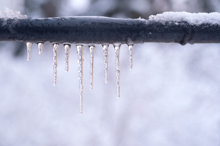 Frozen icicles on a gray pipe after a thaw in winter.